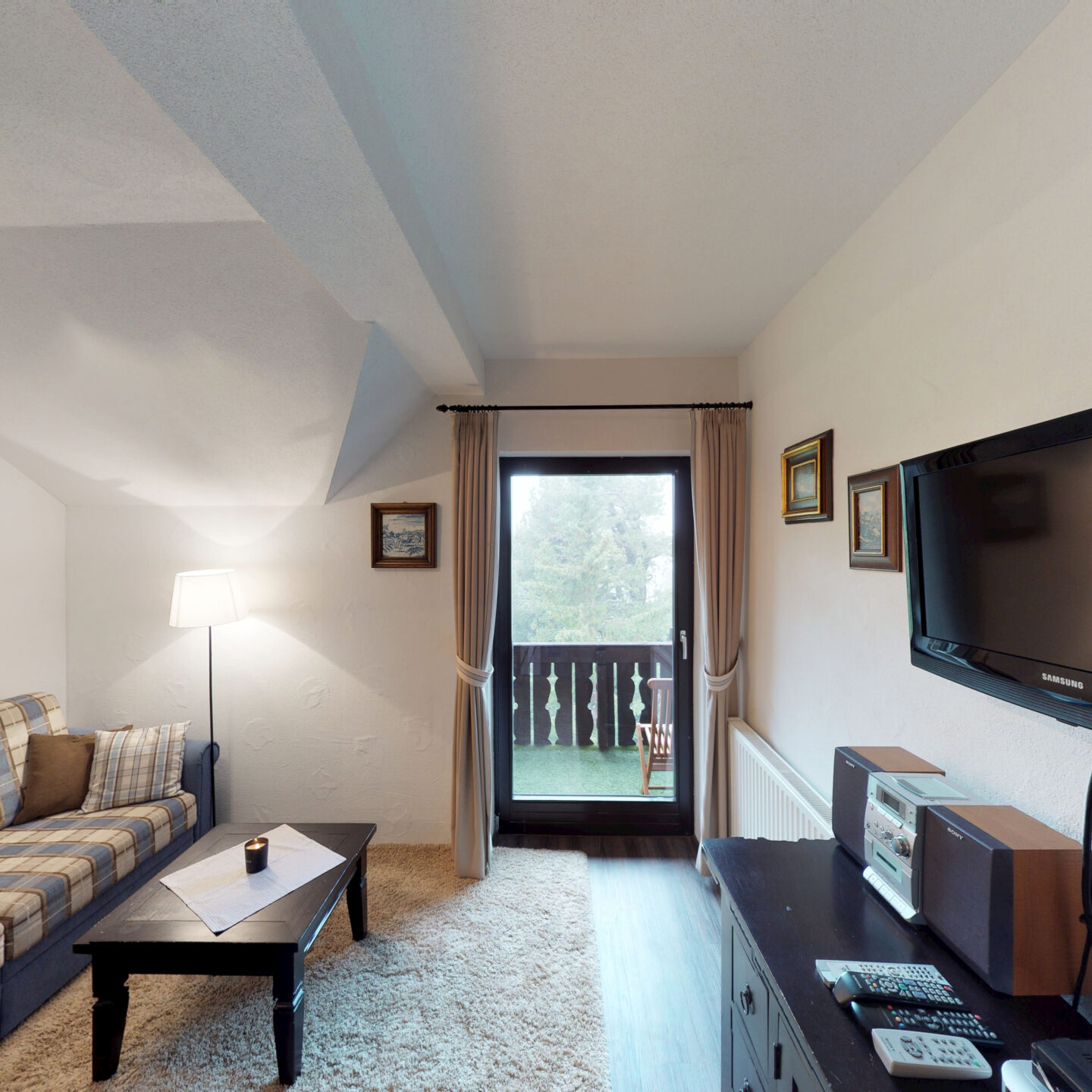 Gemütlicher Wohnraum der Ferienwohnung Wipfelstub’n mit Sitzecke, SAT-TV und Zugang zum Balkon.